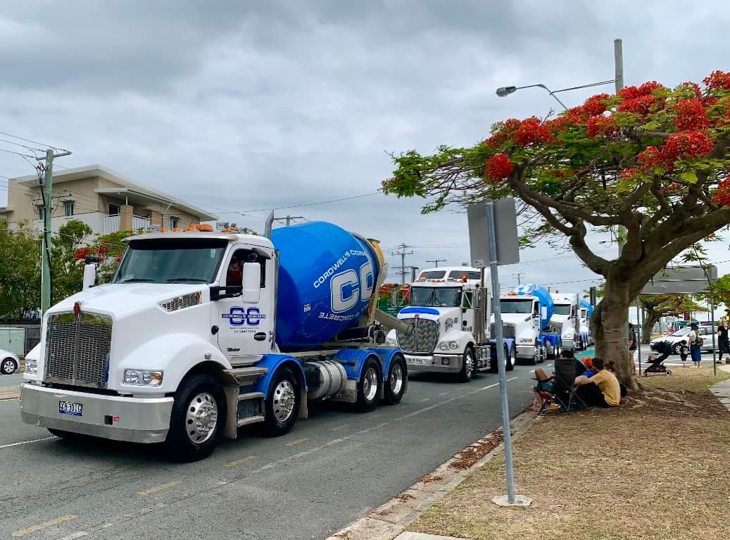 A line of white and blue Cordwells Concrete mixer trucks driving along a street during a community parade.