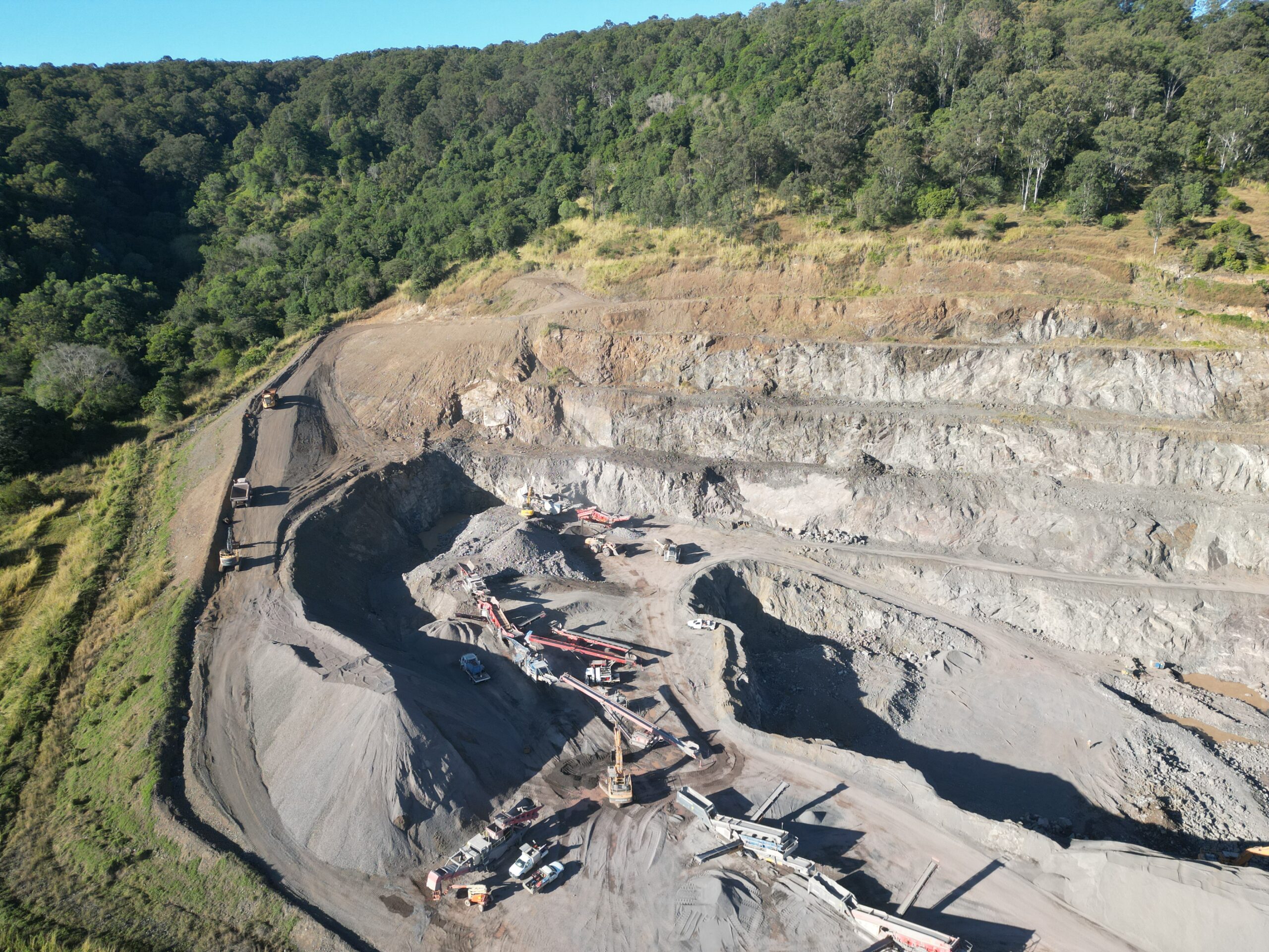 Aerial perspective of a quarry in Noosa, featuring construction machinery and the extraction of rock and aggregates for industry use.
