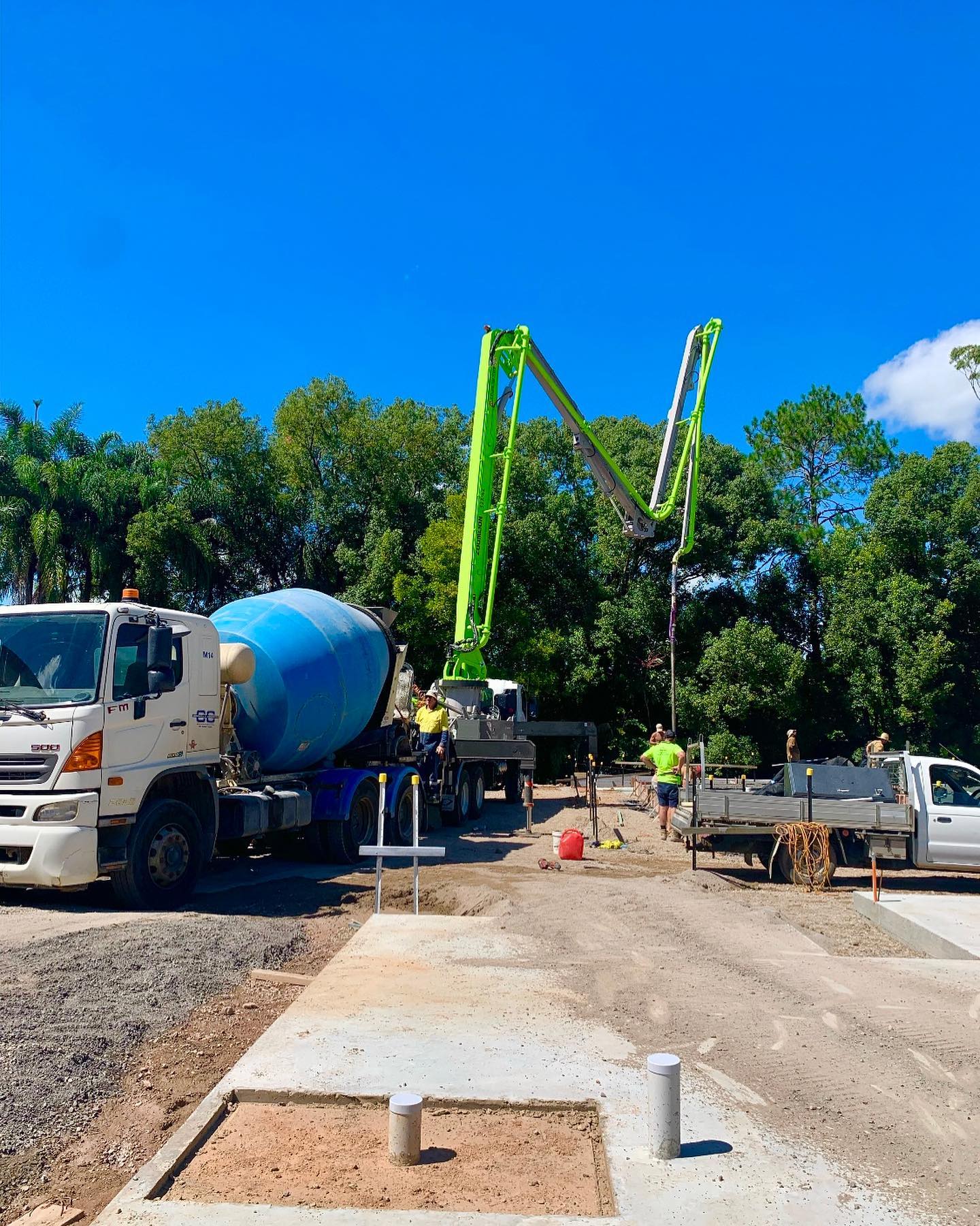 Concrete mixer truck pouring cement onto a construction site slab, with workers overseeing the process in the background.  