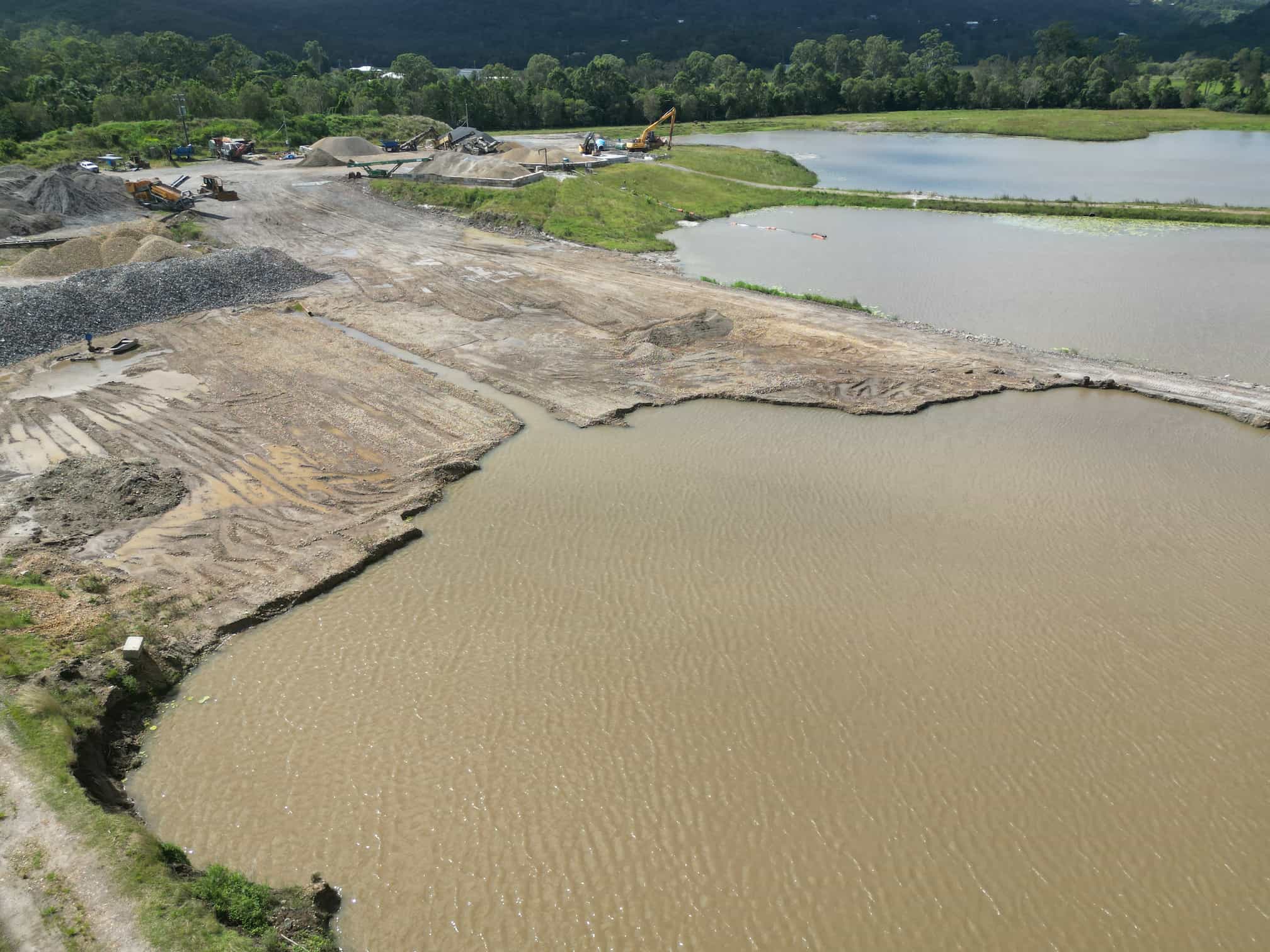 Aerial perspective of a construction site featuring water and dirt, highlighting submerged acid sulphate disposal and monitoring areas.